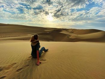 Rear view of woman on sand dune in desert against cloudy sky