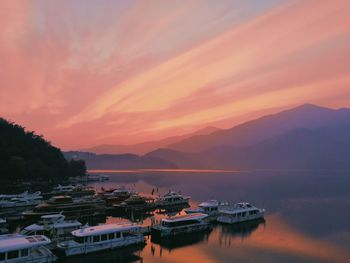 Yachts moored on lake against cloudy sky during sunset