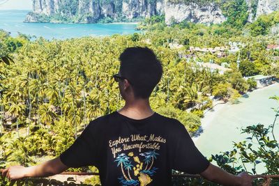 Rear view of young man looking towards palm trees at beach 