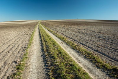 Dirt road amidst field against clear sky