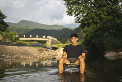 A young handsome asian boy sitting in a chair in the middle of a river, golden hour.