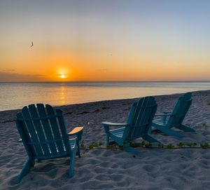 Empty chairs on beach against sky during sunset