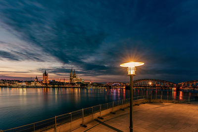 View of cologne cathedral with hohenzollern bridge at nightfall and a lamppost in the foreground, 