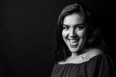 Portrait of smiling young woman against black background