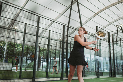 Full length of young woman standing against chainlink fence