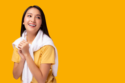 Portrait of smiling young woman against yellow background