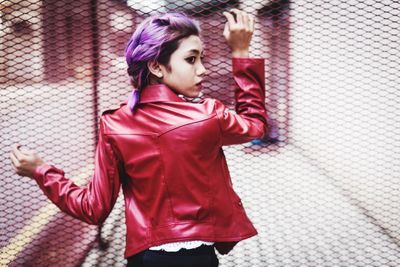 Portrait of young woman standing against pink wall