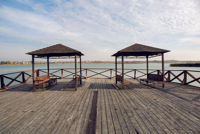 Two gazebos with benches standing on the pier near the lake in autumn
