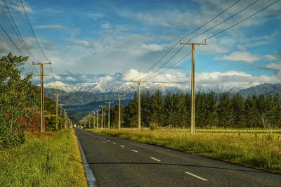 Country road passing through field against cloudy sky