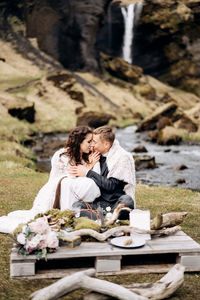 Young couple sitting outdoors against waterfall