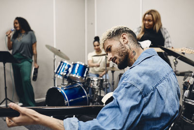 Young man playing guitar while rehearsing with women in classroom