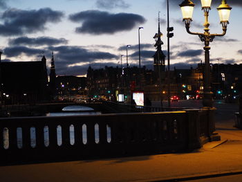 Illuminated street lights in city against sky at dusk