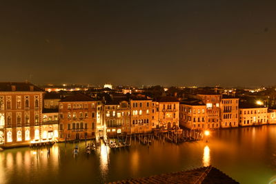 Illuminated buildings by river against sky at night