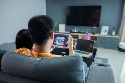 Rear view of man using mobile phone while sitting on sofa