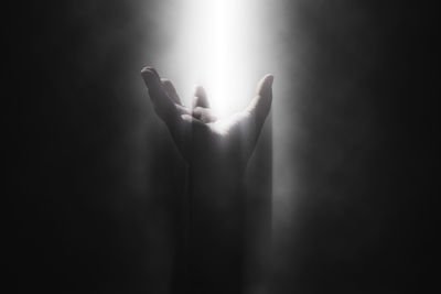 Close-up of hand reaching for light in dark