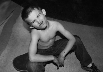 Portrait of shirtless boy sitting on skateboard at street