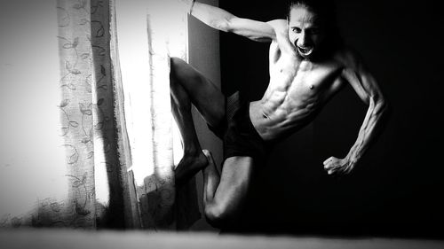 Portrait of young man shouting while climbing on window at home