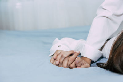 Cropped image of couple holding hands on bed