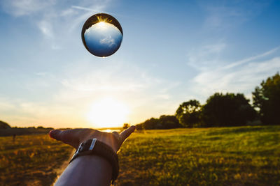 Cropped man catching crystal ball against sky during sunset