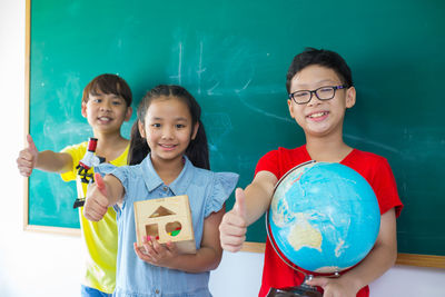 Portrait of smiling students standing against blackboard in classroom