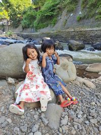 Portrait of girls sitting on rock by river