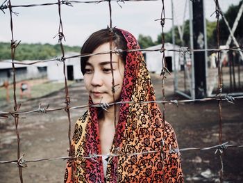 Close-up of young woman standing by chainlink fence