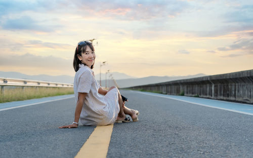 Woman traveler looking at the camera and sitting on the street of the dam with a sunset background 