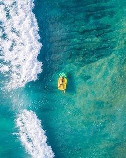 Woman floating on inflatable pineapple in pacific ocean