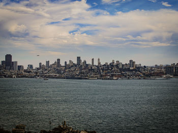 Sea and buildings in city against sky