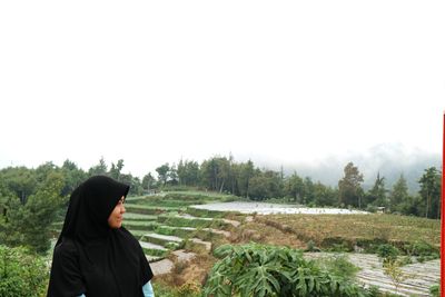 Smiling young woman in hijab looking away against paddy field