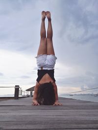 Woman exercising on pier over sea against sky