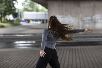 Rear view of young woman dancing on street in city