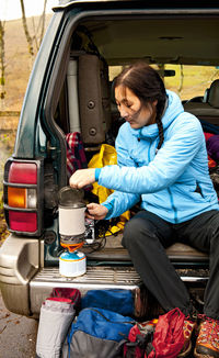 Woman boiling water on camping stove at the back of her car