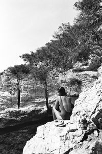 Woman sitting on rock against sky