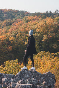 Attractive young man in a black coat and grey cap walks along the rock. wild sarka, prague, czech