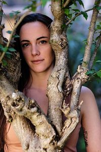 Portrait of young woman standing by tree