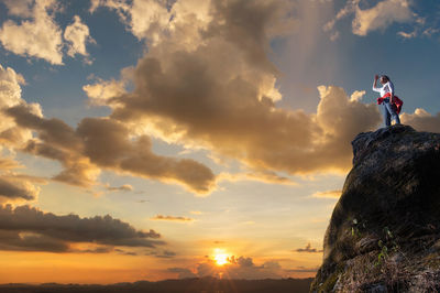 Low angle view of woman standing on rock against sky during sunset