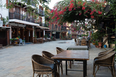 Empty chairs and tables and table and lounge chair and trees and flowers in glasses