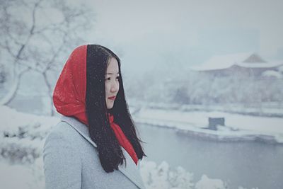 Young woman standing at riverbank during snowfall
