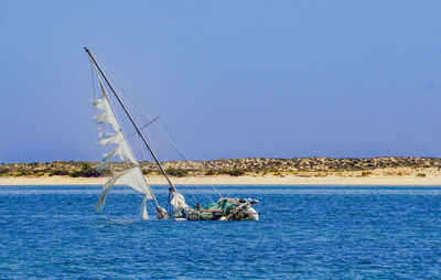 Sailboat sinking on sea against clear sky