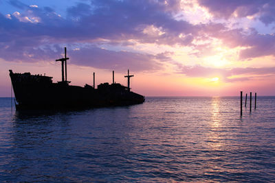 Silhouette wooden posts in sea against sky during sunset