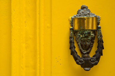 Decorative bronze door knocker in the form of a beautiful woman's head on a yellow painted door