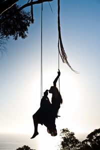 Silhouette of woman kissing bird on swing at sunset