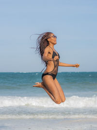 A woman in bikini jumping higher up on the beach