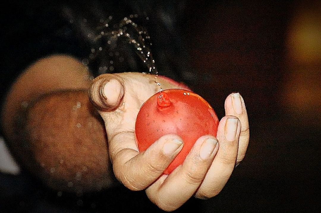 CLOSE-UP OF HAND HOLDING STRAWBERRY OVER BLURRED BACKGROUND