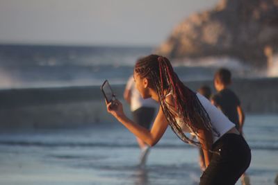 Woman using mobile phone at beach against sky