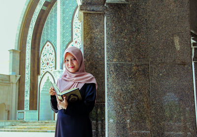 Full length of smiling young woman standing against wall