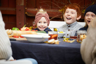 Happy male and female siblings sitting by table for meal