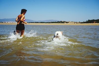 Rear view of woman running in sea with dog