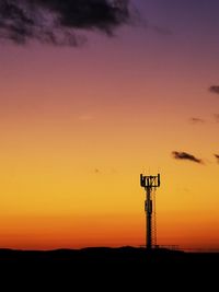 Silhouette tower on field against orange sky